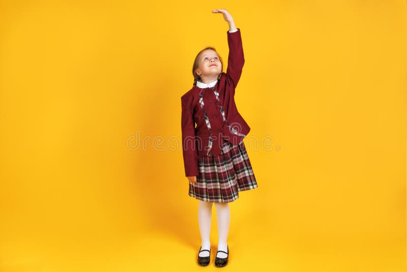 A full-length schoolgirl child in uniform is measuring her height. Little girl on a yellow background stock image A full-length schoolgirl child in uniform is measuring her height. Little girl on a yellow background stock image