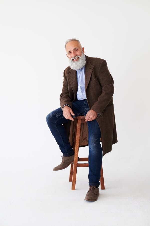 Positive mature bearded man in coat sitting on chair in studio royalty free stock photos Positive mature bearded man in coat sitting on chair in studio royalty free stock photos