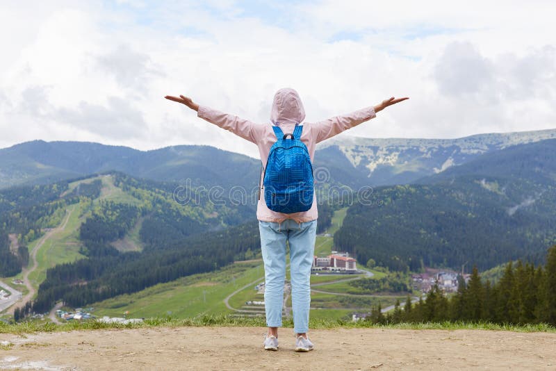 Full length shot of sportive girl hiker going up mountain, standing with arms stretched to sky enjoying landscape, wearing royalty free stock photo Full length shot of sportive girl hiker going up mountain, standing with arms stretched to sky enjoying landscape, wearing royalty free stock photo