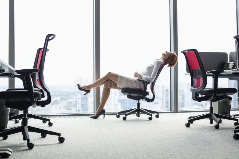 Full length side view of young businesswoman leaning back in chair at office