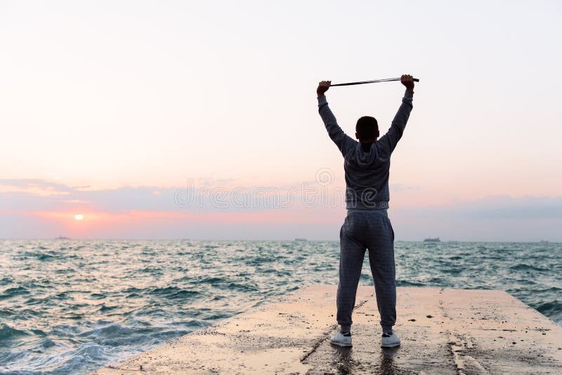 Full length view of sportsman stretching with jump rope, on pier. Full length photo of sportsman practicing exercises, stretching with skipping rope, standing on stock photography Full length view of sportsman stretching with jump rope, on pier. Full length photo of sportsman practicing exercises, stretching with skipping rope, standing on stock photography