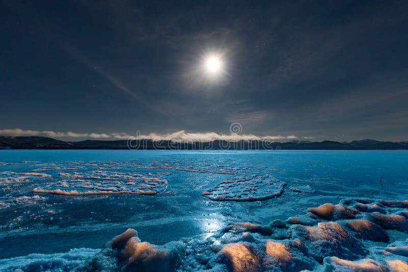 Full moon over frozen Lake Laberge Yukon Canada. Full moon shining over blue ice surface of frozen Lake Laberge, Yukon Territory, Canada