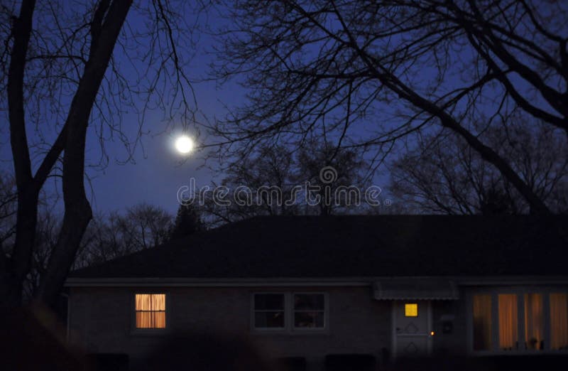 Moon rise over a house with lights on.