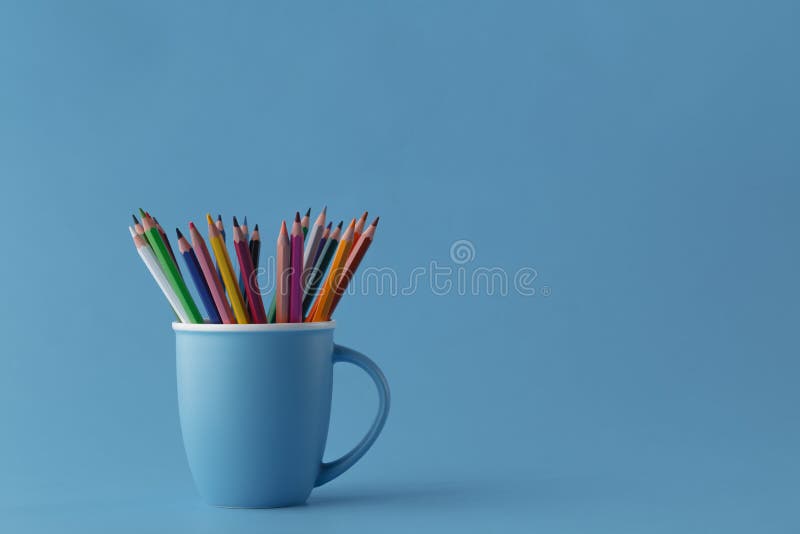 Full mug of sharp color pencils on monochromatic blue background