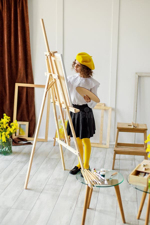 Full size of Cute little artist in yellow beret and tights who paints picture in studio while holds color pallete. Full size of Cute little artist in yellow beret and tights who paints picture in studio while holds color pallete.