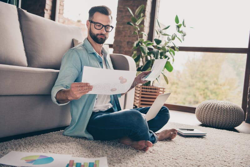 Full size profile side photo of serious focused young bearded man hold laptop documents work sit floor inside house