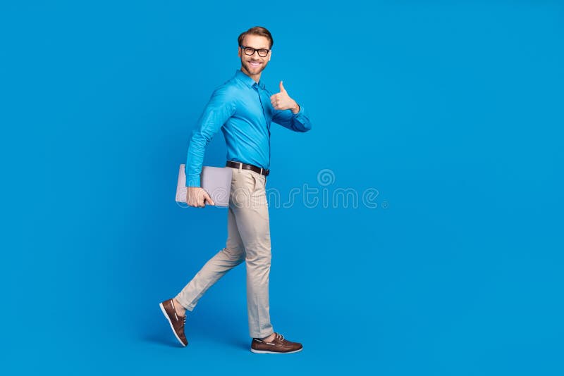 Full size profile side photo of young man happy smile go walk show thumb-up advert advise laptop isolated over blue