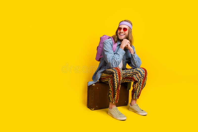 Full size photo of cool young man sit valise look empty space wear denim shirt isolated on yellow color background. Full size photo of cool young man sit valise look empty space wear denim shirt isolated on yellow color background.