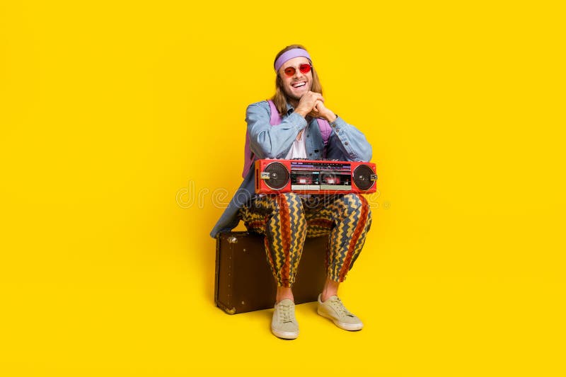 Full size photo of cool young man sit valise boombox empty space wear denim shirt isolated on yellow color background. Full size photo of cool young man sit valise boombox empty space wear denim shirt isolated on yellow color background.