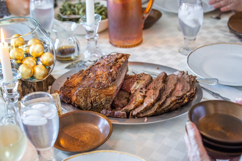 A fully cooked and sliced roast beef celabratory family dinner on the table with a salad bowl and glass of water