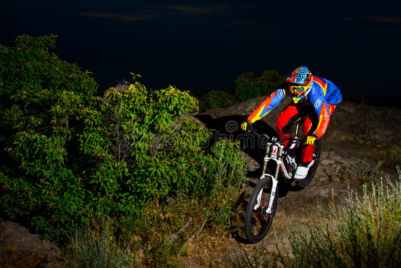 Fully Equipped Professional Downhill Cyclist Riding the Bike on the Night Rocky Trail