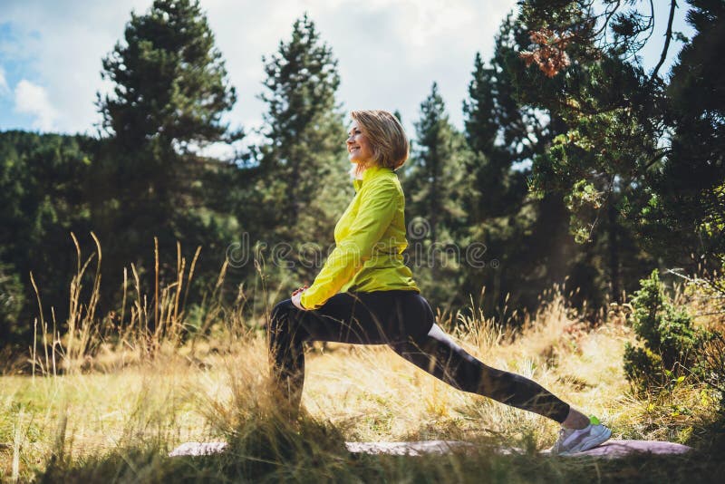 Fun girl one exercising outdoors in green forest sun summer day, activity with stretch legs. Smile fitness woman stretching