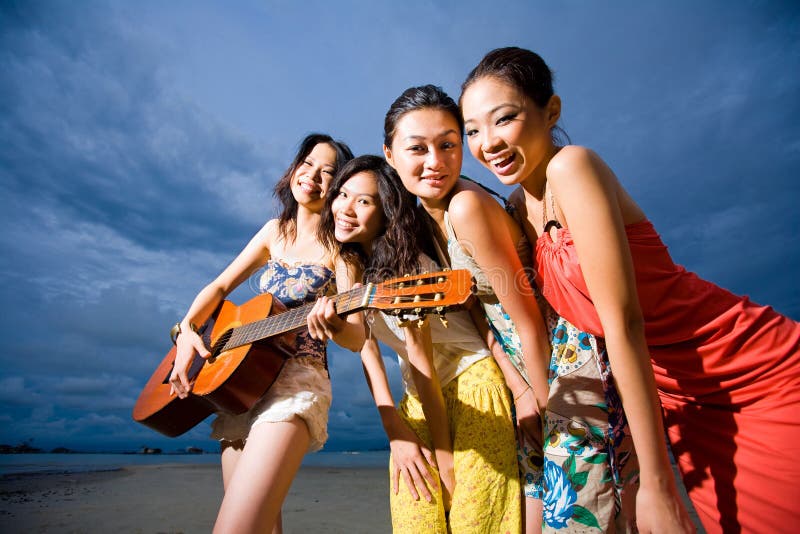 Fun group of girls playing guitar at the beach