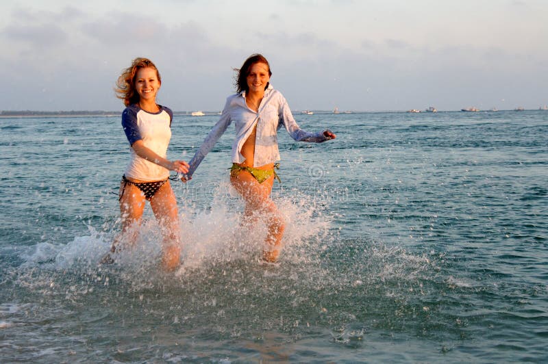 Two young women smiling and running in shallow water close to the beach. Two young women smiling and running in shallow water close to the beach.