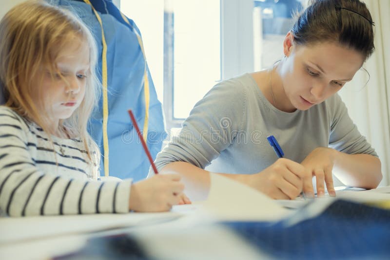 Funcionamento caucasiano da mulher quando sua imagem do desenho da filha perto dela fotografia de stock Funcionamento caucasiano da mulher quando sua imagem do desenho da filha perto dela fotografia de stock