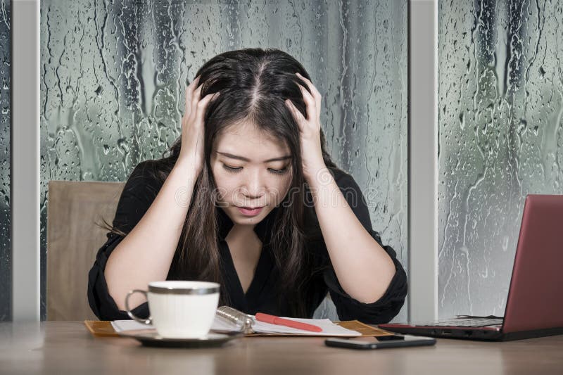 Funcionamiento chino asiático triste y deprimido hermoso joven de la mujer de negocios agotado y frustrado en el escritorio del o fotos de archivo libres de regalías Funcionamiento chino asiático triste y deprimido hermoso joven de la mujer de negocios agotado y frustrado en el escritorio del o fotos de archivo libres de regalías