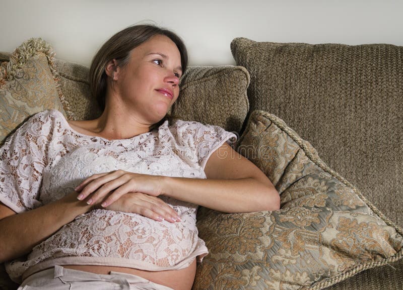 Fundersamt gravid kvinnasammanträde på en soffa arkivbild Fundersamt gravid kvinnasammanträde på en soffa arkivbild