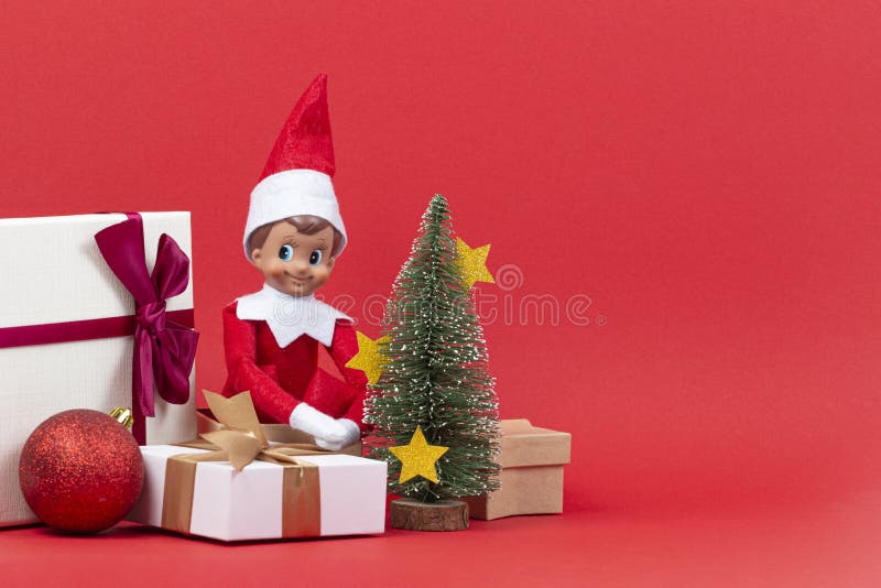 Fundo do Natal Caixas atuais do Xmas, árvore pequena do Xmas com decorações e duende do brinquedo no fundo vermelho fotografia de stock Fundo do Natal Caixas atuais do Xmas, árvore pequena do Xmas com decorações e duende do brinquedo no fundo vermelho fotografia de stock