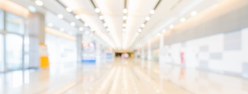 Blurred bokeh panoramic banner background of exhibition hall or convention center hallway. Business trade show event, modern interior architecture, or commercial tradeshow conference seminar concept. Blurred bokeh panoramic banner background of exhibition hall or convention center hallway. Business trade show event, modern interior architecture, or commercial tradeshow conference seminar concept