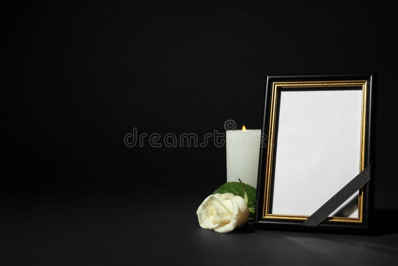 Funeral photo frame with ribbon, white rose and candle on table against black background. Space for design