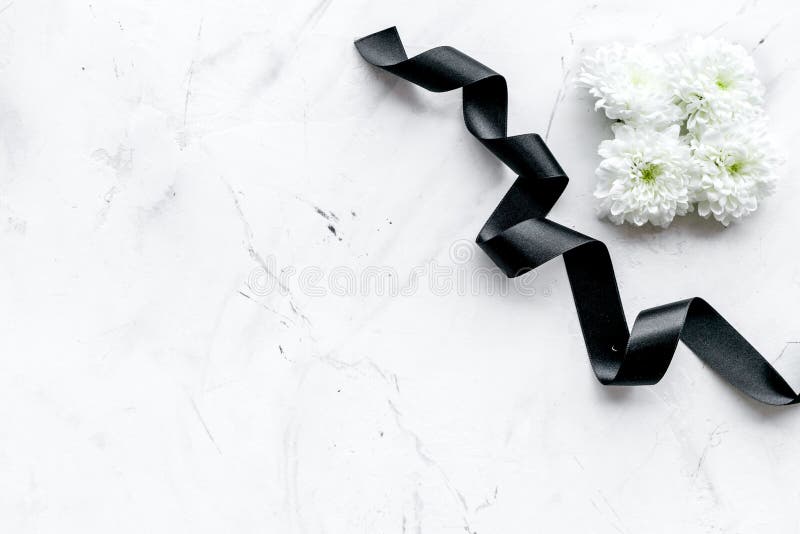 Funeral symbols. White flower near black ribbon on white stone background top view copy space
