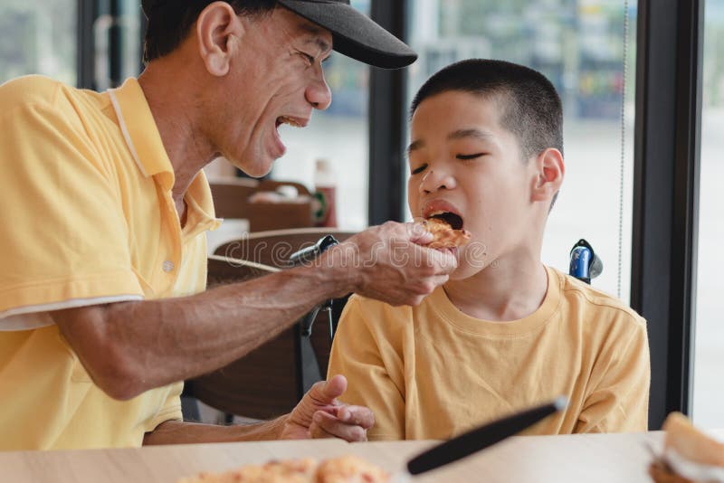 Father feeding food to Disabled child on the wheelchair in pizza shop, He practiced eating food, Special children`s lifestyle, Lifestyle in the education age of kids, Happy disability kid concept. Father feeding food to Disabled child on the wheelchair in pizza shop, He practiced eating food, Special children`s lifestyle, Lifestyle in the education age of kids, Happy disability kid concept