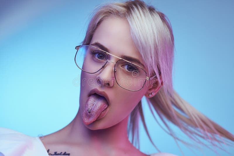 Funky blonde girl wearing glasses poses with tongue sticking out looking at...