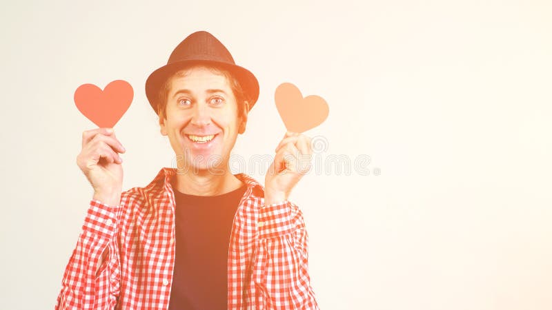 Funky crazy cheerful guy holding red hearts. Man in love. Copy space. Funny man in black hat and plaid shirt, isolated on white. stock photo Funky crazy cheerful guy holding red hearts. Man in love. Copy space. Funny man in black hat and plaid shirt, isolated on white. stock photo