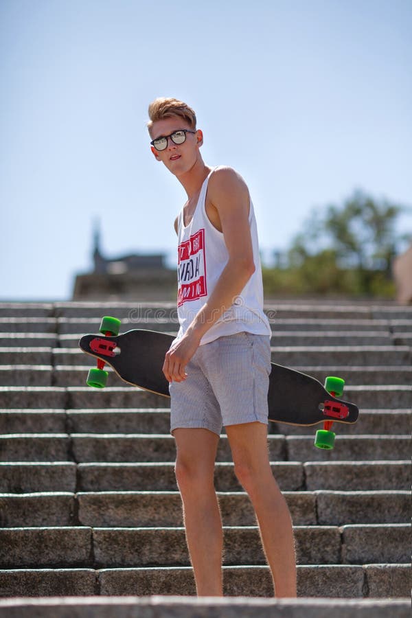 Trendy handsome young man with a skateboard on street stairs background. Active lifestyle and youth concept. Copy space.