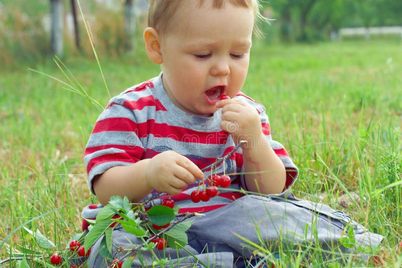 Funny baby boy eating fresh ripe cherry