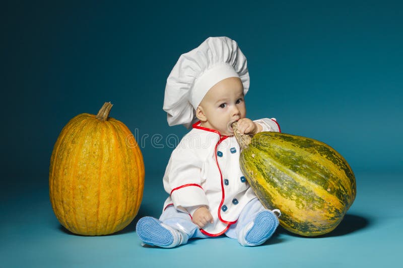 Funny baby with cook costume holds pumpkin
