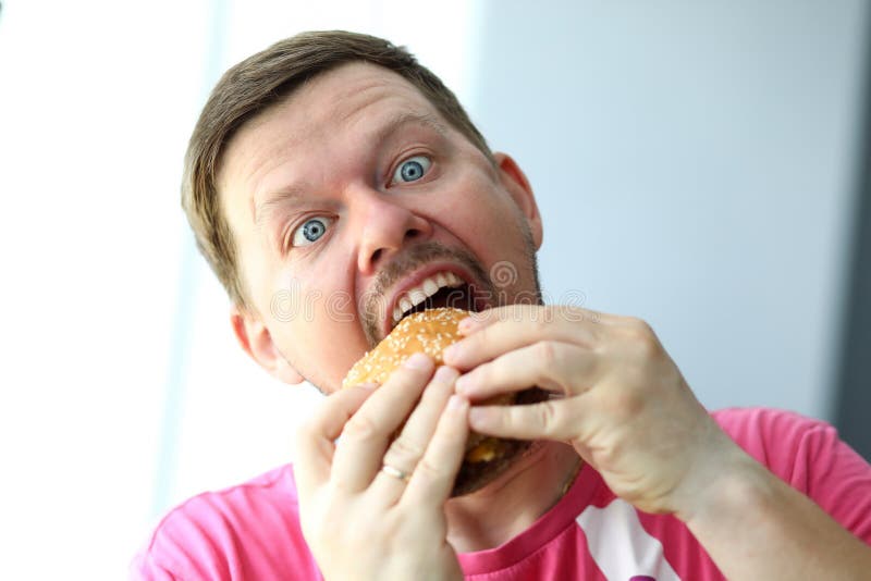 Funny bearded man with idiot facial expression eating burger stock photo Funny bearded man with idiot facial expression eating burger stock photo