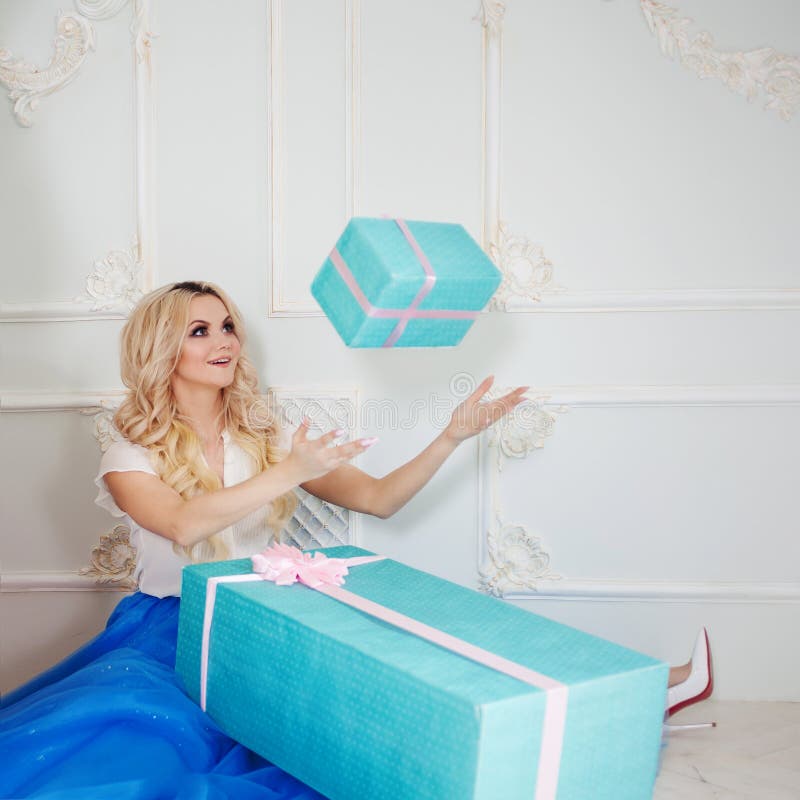 Funny and beautiful blonde with huge gift box. Charming young woman in a curvy blue skirt. royalty free stock photo Funny and beautiful blonde with huge gift box. Charming young woman in a curvy blue skirt. royalty free stock photo