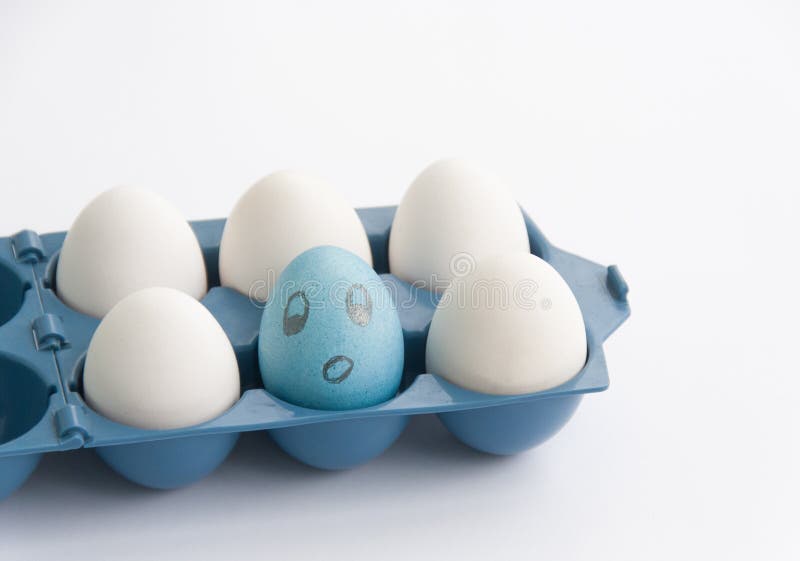 Funny Blue Egg With Face Among Other White Eggs In Blue Plastic