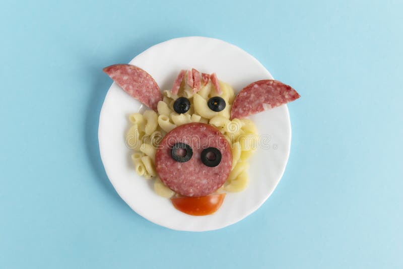 Funny Breakfast, lunch or dinner for children in the form of a bull`s face made of pasta, sausage, bacon, olives and fresh tomatoes on a blue background. Instruction how to make creative food art breakfast for kids. Step 7. Top view. Funny Breakfast, lunch or dinner for children in the form of a bull`s face made of pasta, sausage, bacon, olives and fresh tomatoes on a blue background. Instruction how to make creative food art breakfast for kids. Step 7. Top view