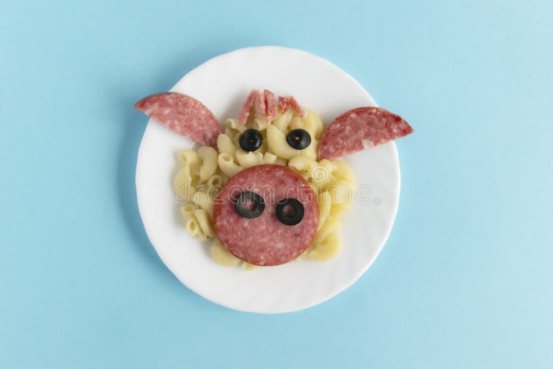 Funny Breakfast, lunch or dinner for children in the form of a bull`s face made of pasta, sausage, bacon, olives and fresh tomatoes on a blue background. Instruction how to make creative food art breakfast for kids. Step 6. Top view. Funny Breakfast, lunch or dinner for children in the form of a bull`s face made of pasta, sausage, bacon, olives and fresh tomatoes on a blue background. Instruction how to make creative food art breakfast for kids. Step 6. Top view