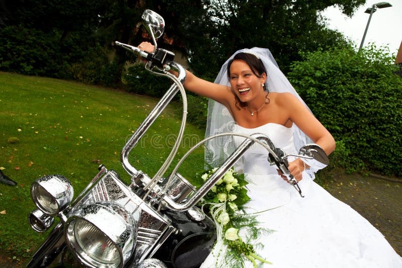 Funny bride well know as bride chick is laughing and sitting on a Harley Davidson bike after her wedding ceremony. Funny bride well know as bride chick is laughing and sitting on a Harley Davidson bike after her wedding ceremony