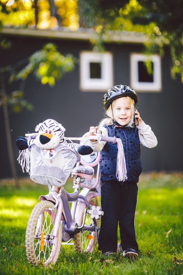 Funny child Caucasian girl blonde in a bicycle helmet near a purple bike with a basket in outside the park on a green royalty free stock photo Funny child Caucasian girl blonde in a bicycle helmet near a purple bike with a basket in outside the park on a green royalty free stock photo