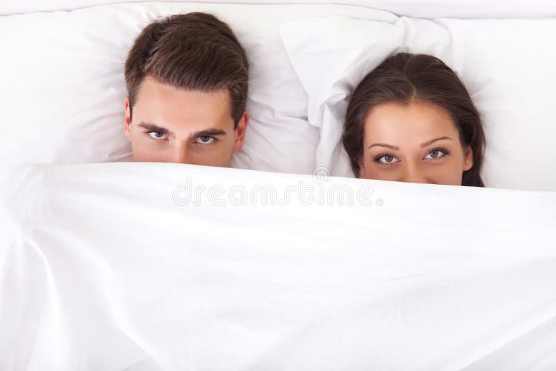 Funny couple lying in bed with the sheet pulled up over their noses. Funny couple lying in bed with the sheet pulled up over their noses