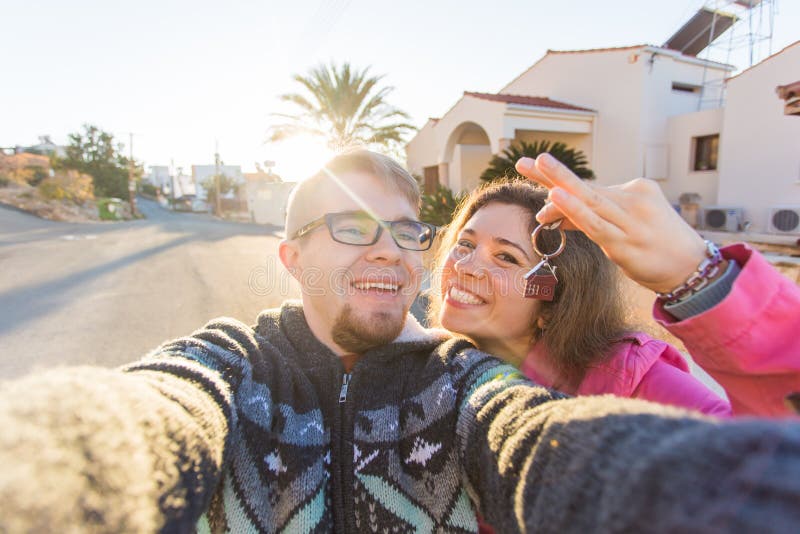 Funny couple With Keys Standing Outside New Home. Real estate, owner and people concept