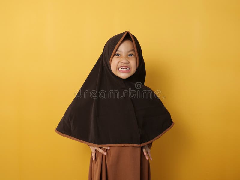 Funny cute Asian muslim little girl wearing hijab looked angry and upset, looking at camera, against yellow stock photo