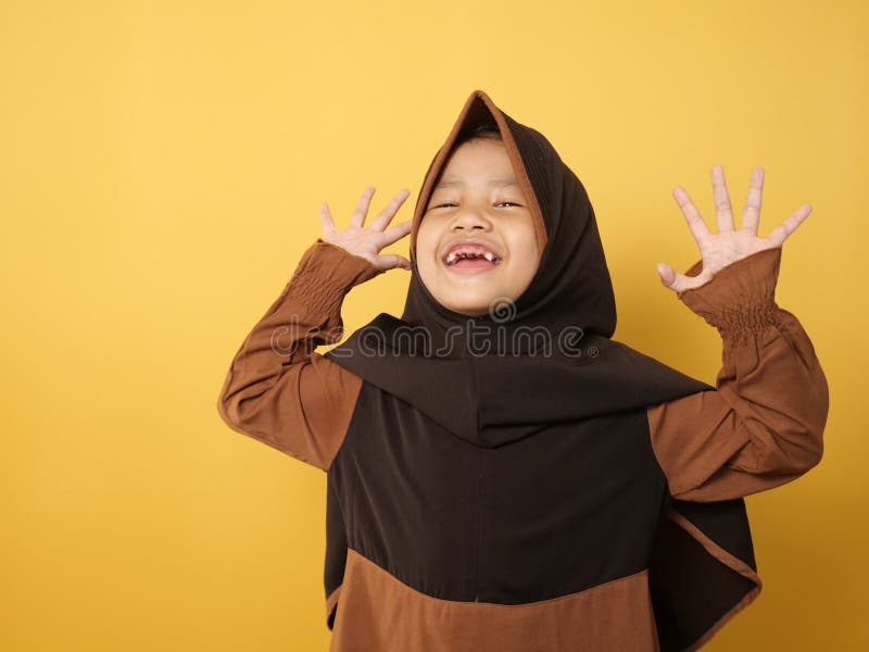 Funny cute Asian muslim little girl wearing hijab looked happy and laughing, against yellow stock images