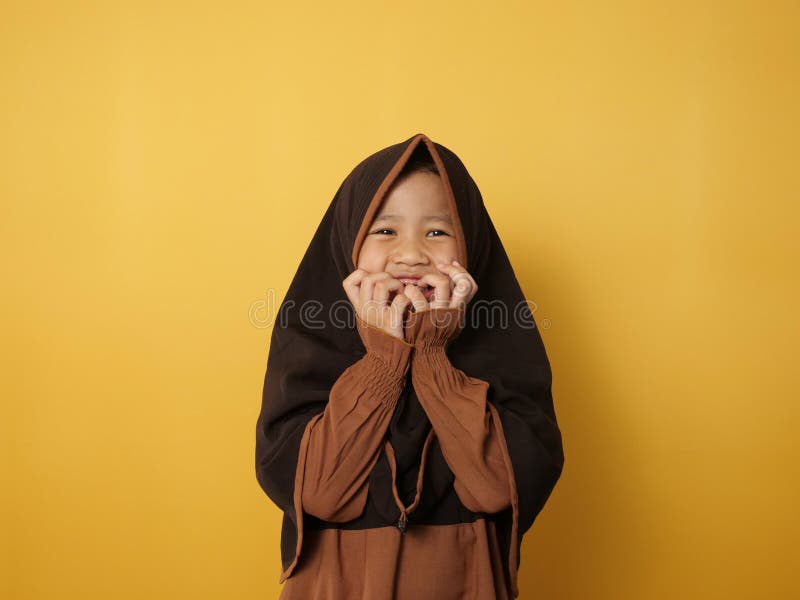 Funny cute Asian muslim little girl wearing hijab looked shocked and scared covering his mouth, against yellow royalty free stock image