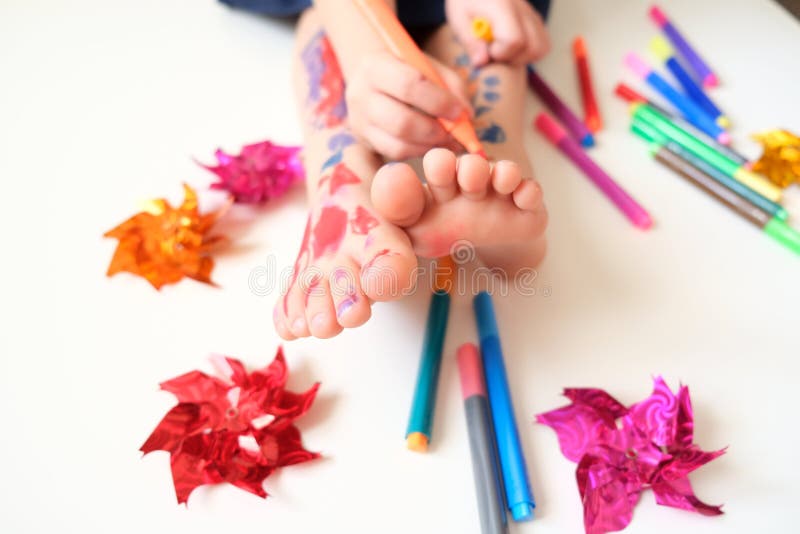 Close up hand brush drawing funny face on feet children with painted toes.  Baby art therapy