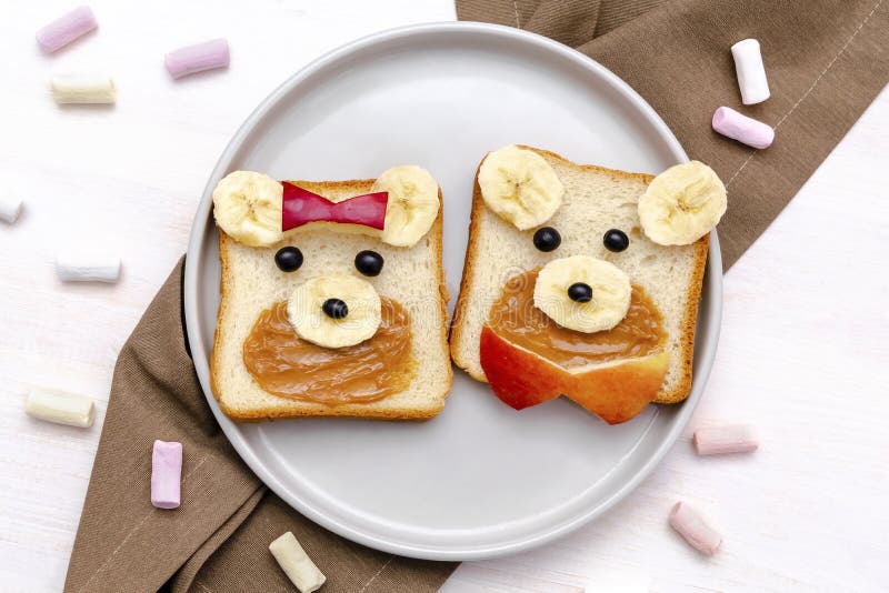 Funny cute bear,dog faces sandwich toast bread with peanut butter, banana, apple, marshmallow. Kids childrens baby's sweet dessert healthy breakfast lunch food art on plate,close up,top view. Funny cute bear,dog faces sandwich toast bread with peanut butter, banana, apple, marshmallow. Kids childrens baby's sweet dessert healthy breakfast lunch food art on plate,close up,top view