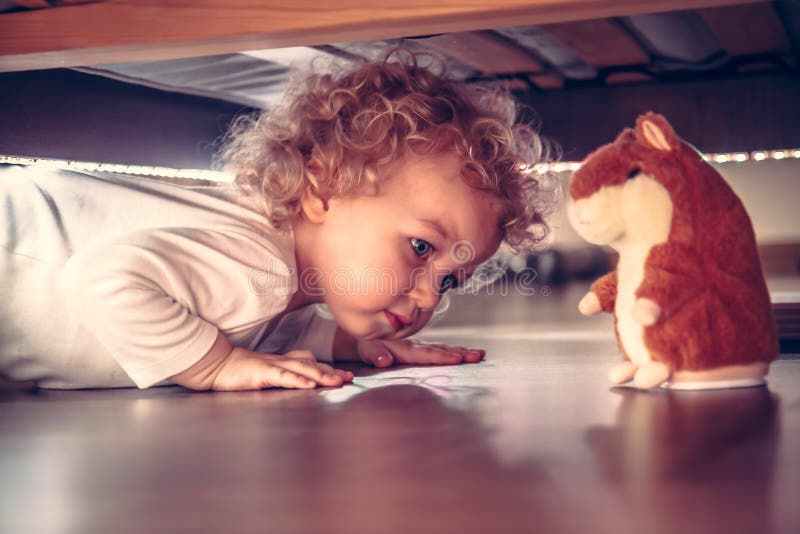 Funny cute curious baby playing under the bed with toy hamster in vintage style royalty free stock photo