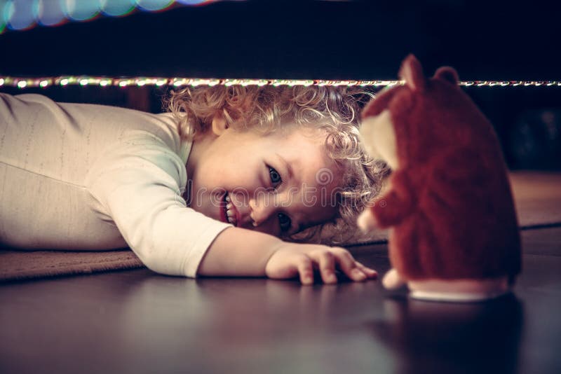Funny cute smiling baby playing hide and seek under the bed with toy hamster in vintage style royalty free stock photo