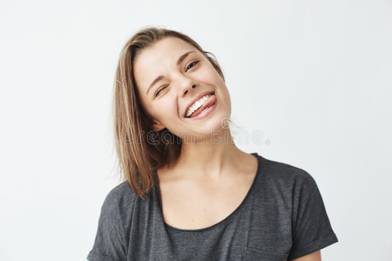 Funny cute young girl smiling winking showing tongue looking at camera over white background.