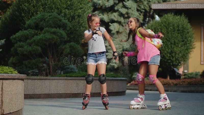 Funny dance of two young girls roller skating in a city park