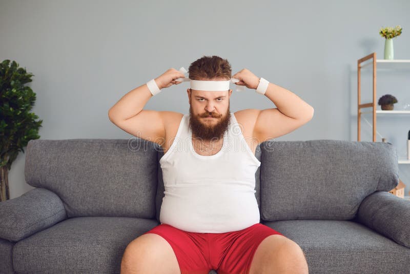Funny Fat Man In Sportswear Is Sitting On The Sofa In The Room Stock